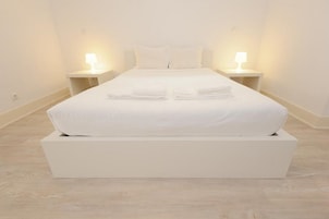 Una cama grande con sábanas blancas y dos mesitas de noche con lámparas.