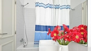 A bathroom with a shower, a white bathtub, and a vase of red flowers on the counter. - Portugal Ways Lisbon City Apartments (Lisbon)