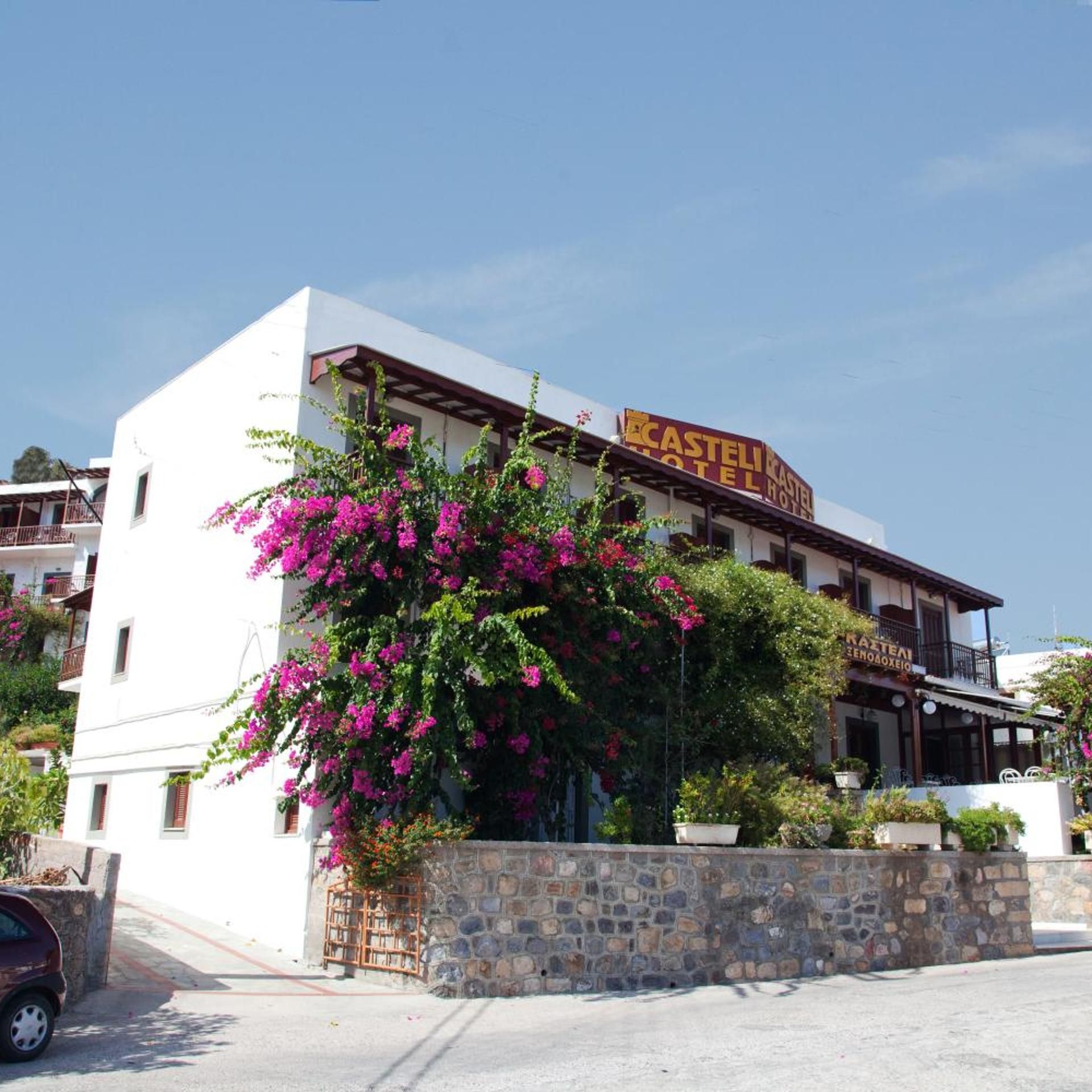 A hotel with a white facade, a stone wall, and a sign that reads 'CASTELI HOTEL.'