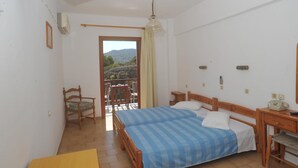 A bedroom with a bed, a wooden desk, a chair, a small table, a ceiling fan, and a window with a view of the outdoors. - Castelli (Patmos)