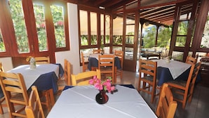A covered dining area with tables and chairs, large windows, and a view of greenery outside. - Castelli (Patmos)