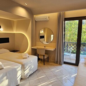 A hotel room with a bed, a desk, a chair, a round mirror, and a balcony with a view of trees. - Olympic Village (Archaia Olympia)