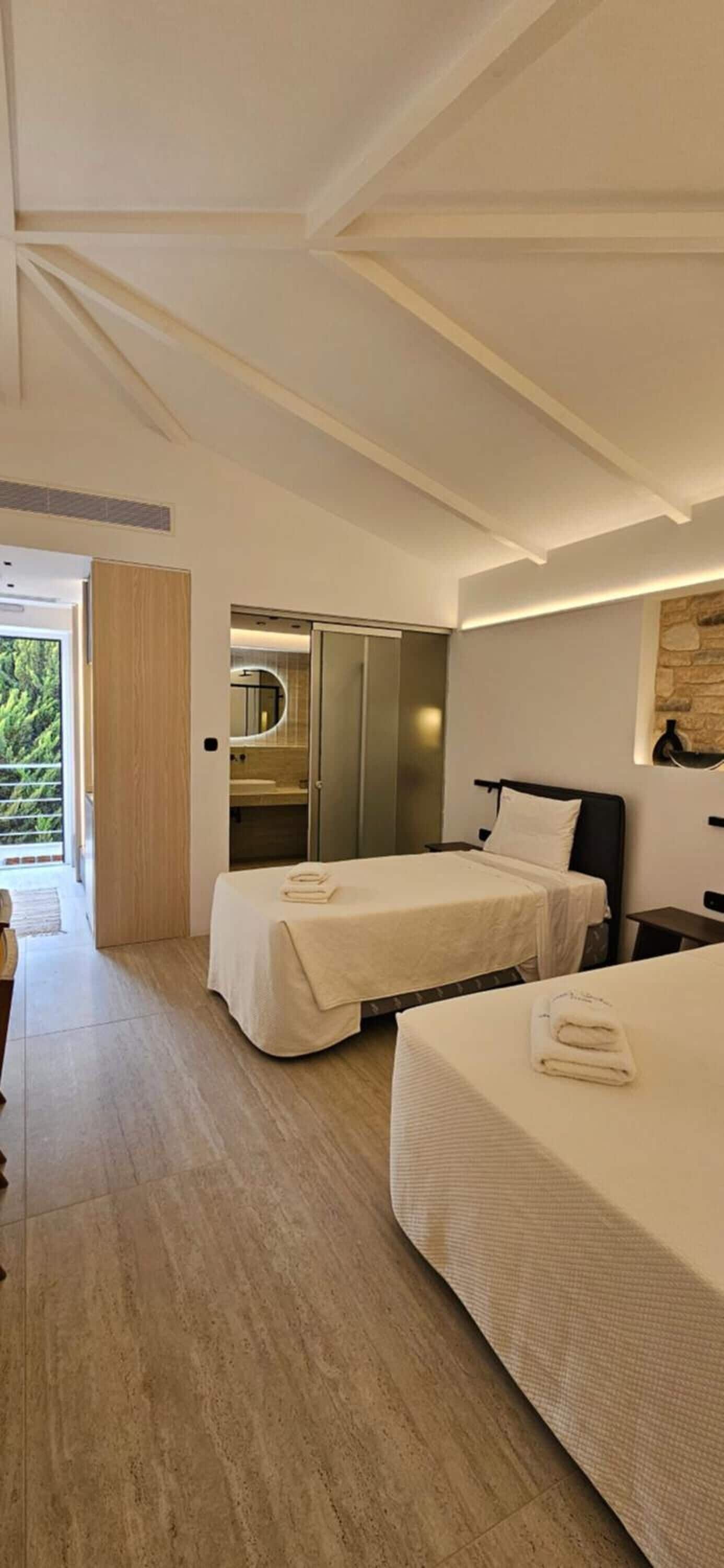Habitación de hotel moderna con dos camas, un baño con espejo y vistas a zonas verdes.