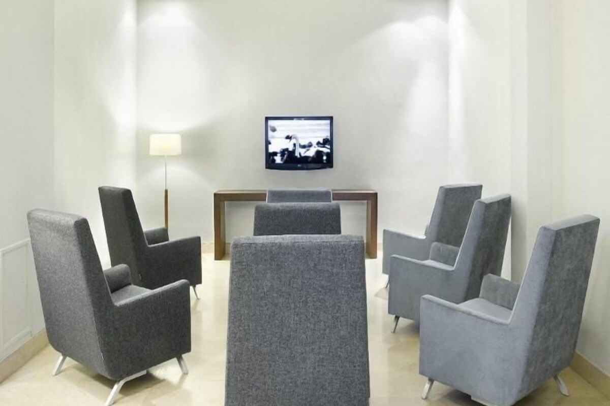 Ein Hotelzimmer mit einer Sitzecke, ausgestattet mit vier grauen Sesseln und einem an der Wand befestigten Fernseher.