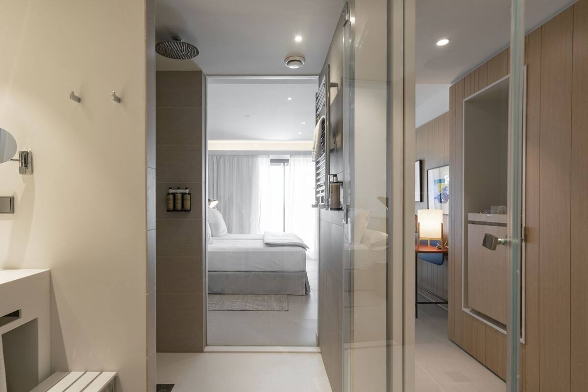 A modern hotel room with a bed, a bathroom, and a desk with a lamp.