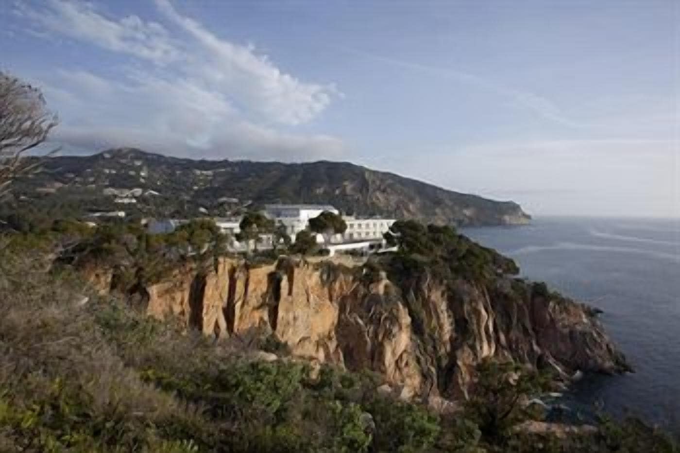 Une propriété située sur la côte, avec vue sur une falaise, comprenant un grand bâtiment et donnant sur une étendue d’eau.
