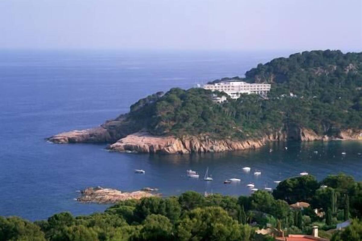 A coastal hotel with a view of the sea, surrounded by greenery and a rocky coastline.