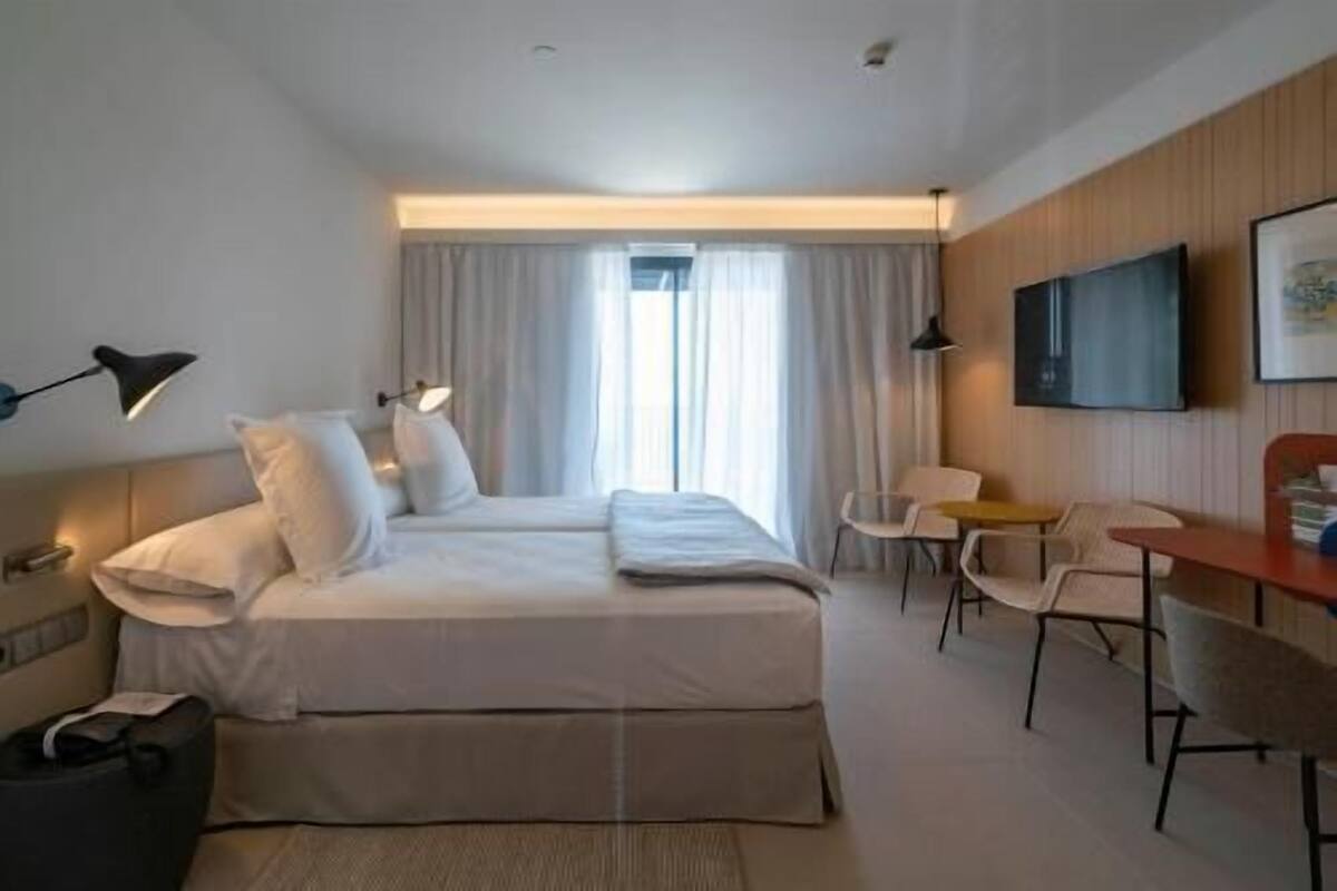 A modern hotel room with a bed, bedside lamps, a desk, and a chair.