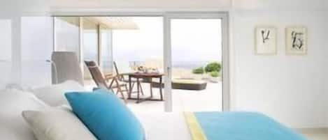A modern hotel room with a bed, a view of the beach, and a dining area.