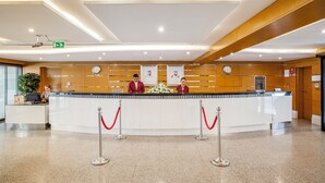A reception desk with two staff members, a clock, and a bulletin board. - Golden Sands Hotel Apartments (Dubai)