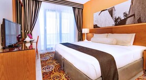A hotel room with a large bed, a television on a wooden desk, a desk lamp, and a framed picture on the wall. - Golden Sands Hotel Apartments (Dubai)