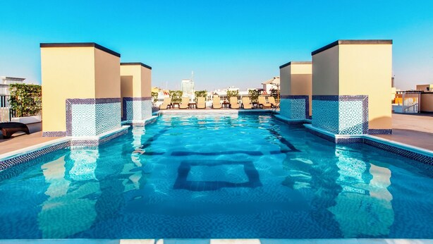 Ein Schwimmbecken mit gefliesten Rändern, umgeben von beigen Säulen und einem klaren, blauen Himmel.