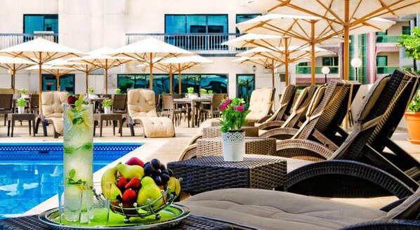 Zona de piscina con sillones de descanso, sombrillas y un frutero.