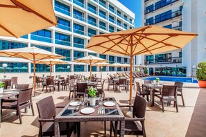 An outdoor dining area with tables and chairs, umbrellas, and a pool in the background. - Golden Sands Hotel Apartments (Dubai)