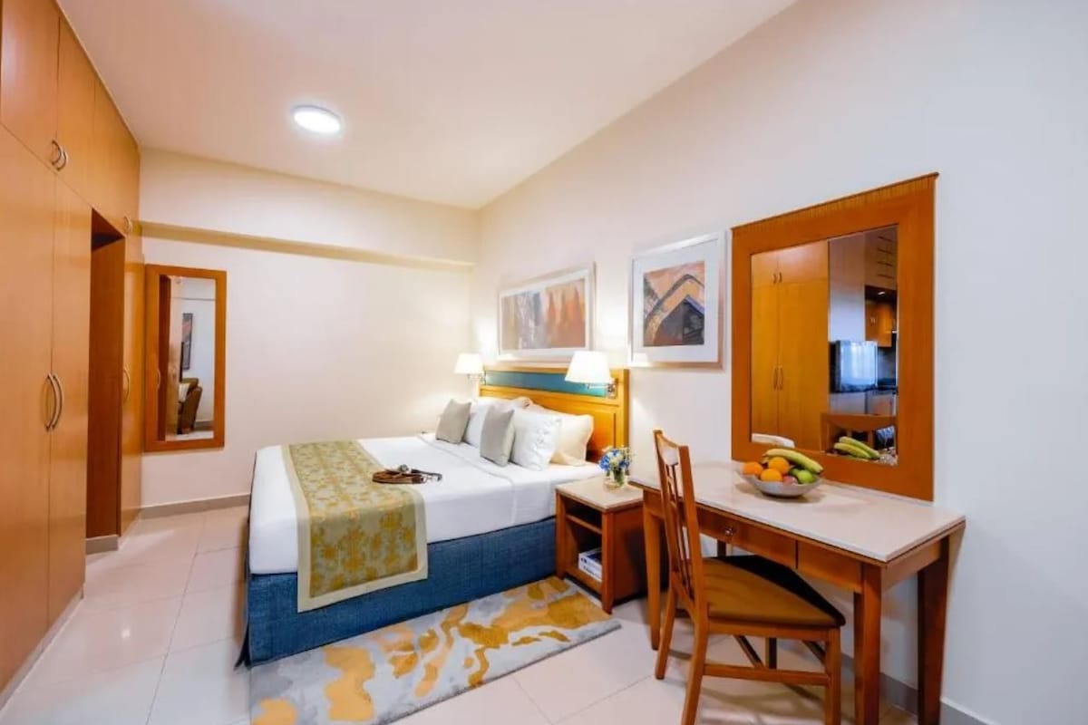 A hotel room with a bed, bedside table, chair, desk, and a mirror.
