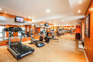 A gym with treadmills, weight machines, and a television screen.