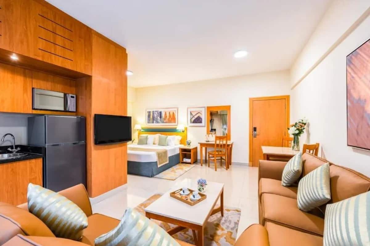 A modern hotel room with a kitchenette, a bed, a dining area, and a living room.