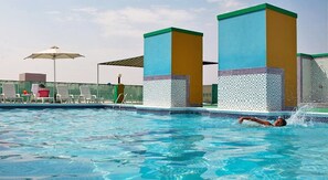 A swimming pool with a person swimming, lounge chairs, and a covered area. - Golden Sands Hotel Apartments (Dubai)