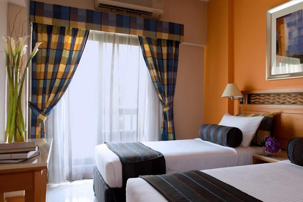 A hotel room with two beds, a bedside table, a lamp, and a window with curtains.