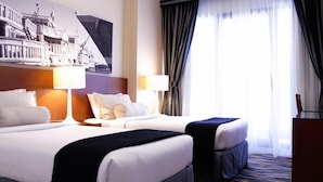 A hotel room with two beds, a large window with curtains, and a wall-mounted artwork. - Golden Sands Hotel Apartments (Dubai)