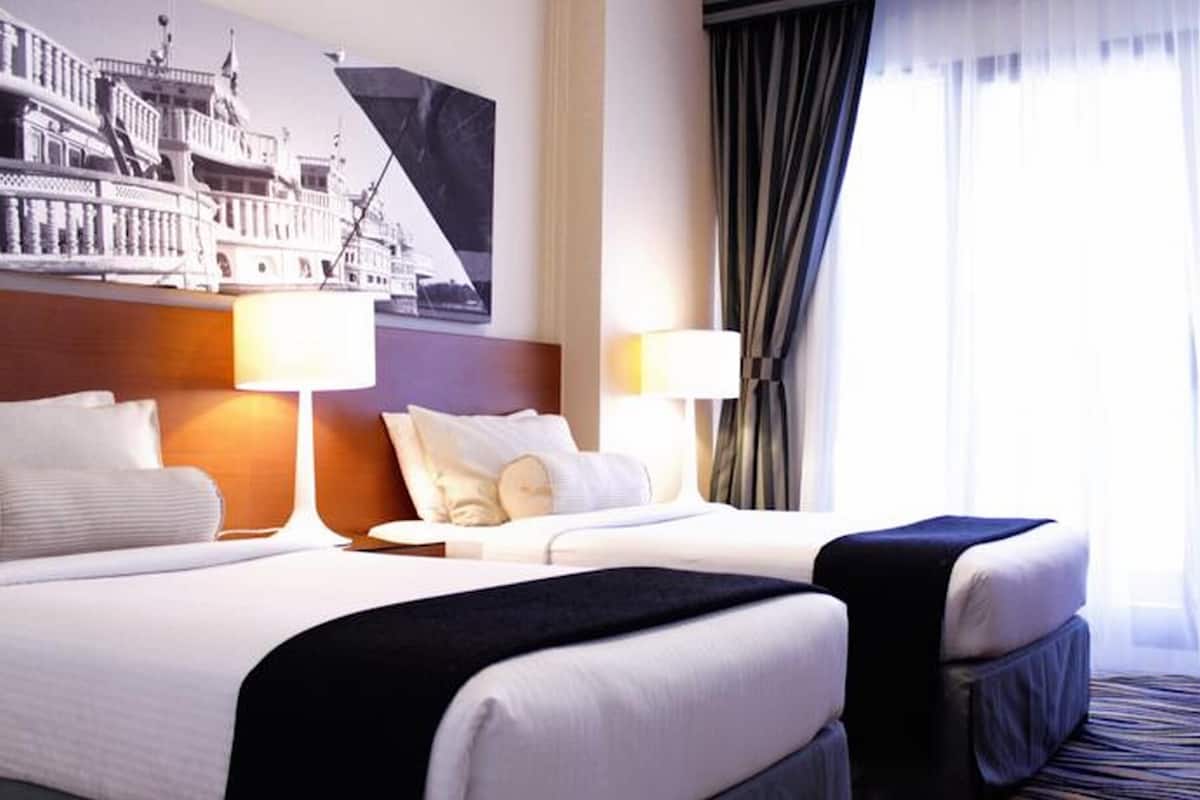 A hotel room with two beds, a large window with curtains, and a wall-mounted artwork.