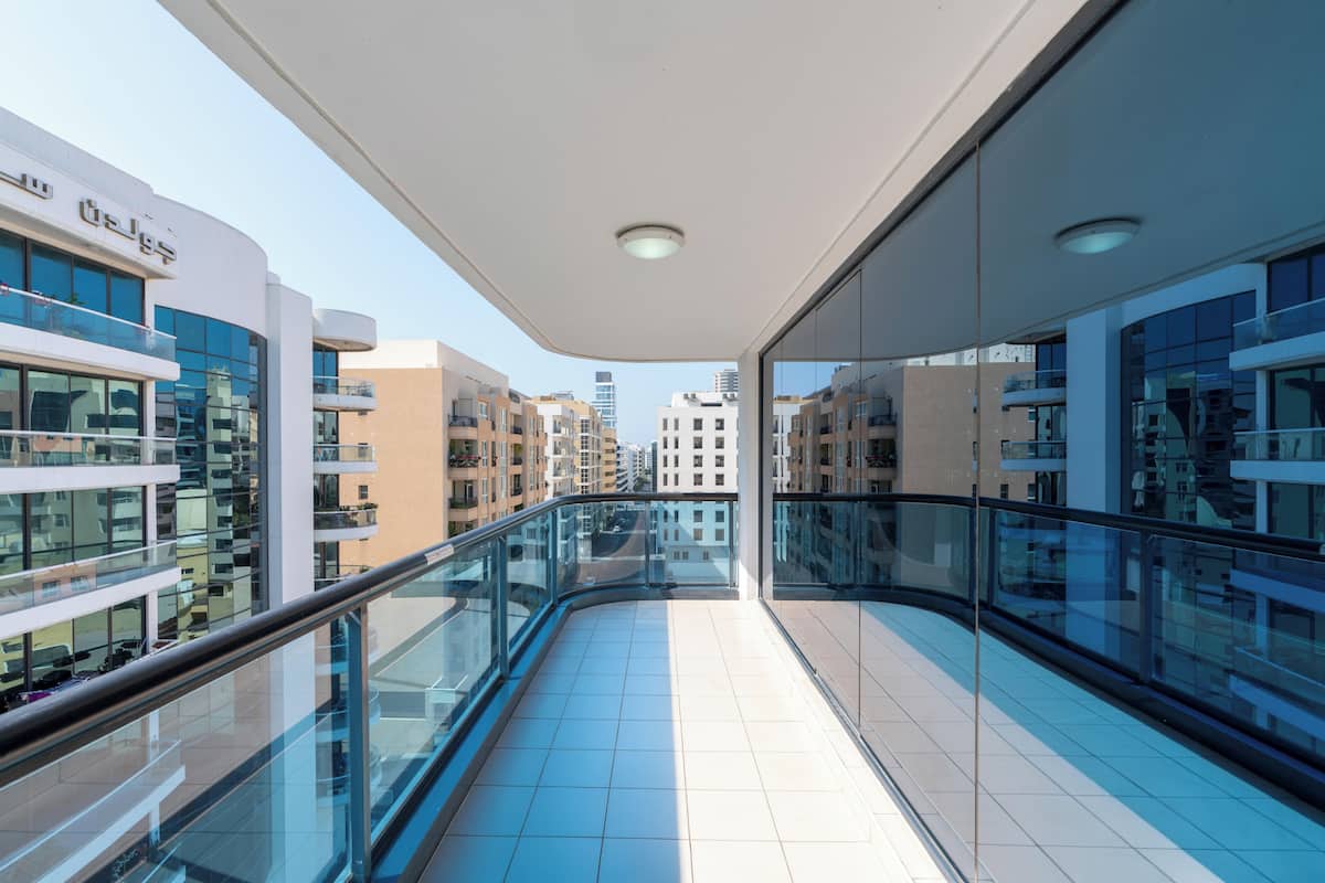 A modern building with a glass balcony, reflective glass walls, and a tiled floor.