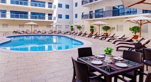 Zona junto a la piscina con sillas de descanso, sombrillas y una mesa de comedor para dos.