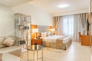 A hotel room with a bed, a sofa, a nightstand with lamps, a small table, and a TV.