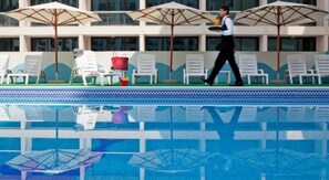 Zona de piscina con sillones de descanso, sombrillas y una persona caminando con una bandeja.