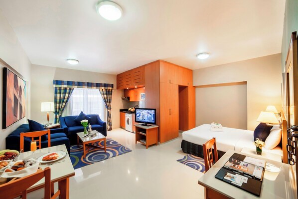 A hotel room with a bed, a sofa, a TV, a dining table, and a small kitchen area. - Golden Sands Hotel Apartments (Dubai)