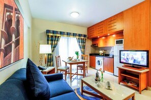 Una sala de estar con sofá, mesa de centro, televisor y un área de cocina con armarios de madera y electrodomésticos.