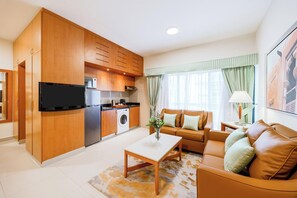 A modern kitchen with wooden cabinets, a built-in oven, and a washing machine. There is a living area with a sofa and a coffee table. - Golden Sands Hotel Apartments (Dubai)
