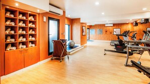 A gym with exercise equipment, a massage chair, and a wall with shelves of towels. - Golden Sands Hotel Apartments (Dubai)