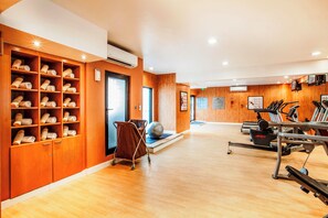 A gym with exercise equipment, a massage chair, and a wall with shelves of towels. - Golden Sands Hotel Apartments (Dubai)