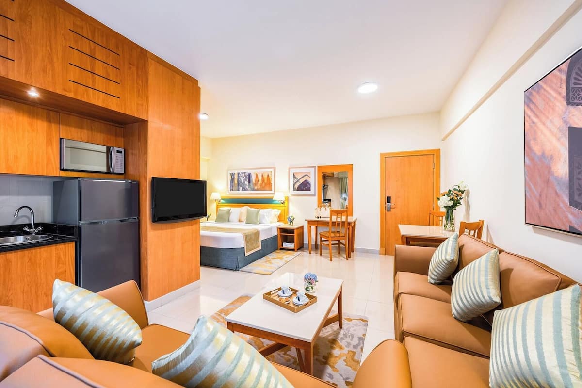 A modern hotel room with a kitchenette, a bed, a dining area, and a living room.