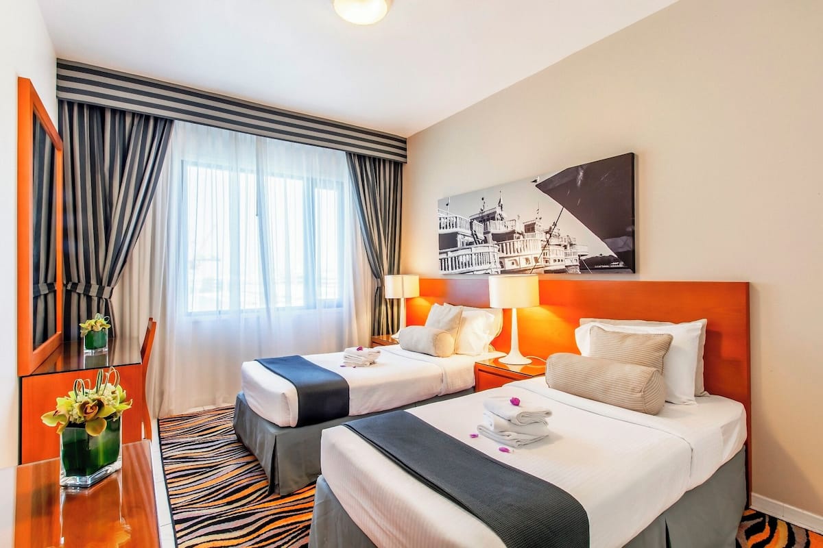 A hotel room with two beds, a mirror, a desk, and a window with curtains.