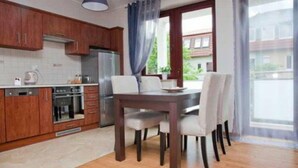 A modern kitchen with wooden cabinets, a dining table with chairs, and a large window with curtains. - Molo Apartments (Sopot)