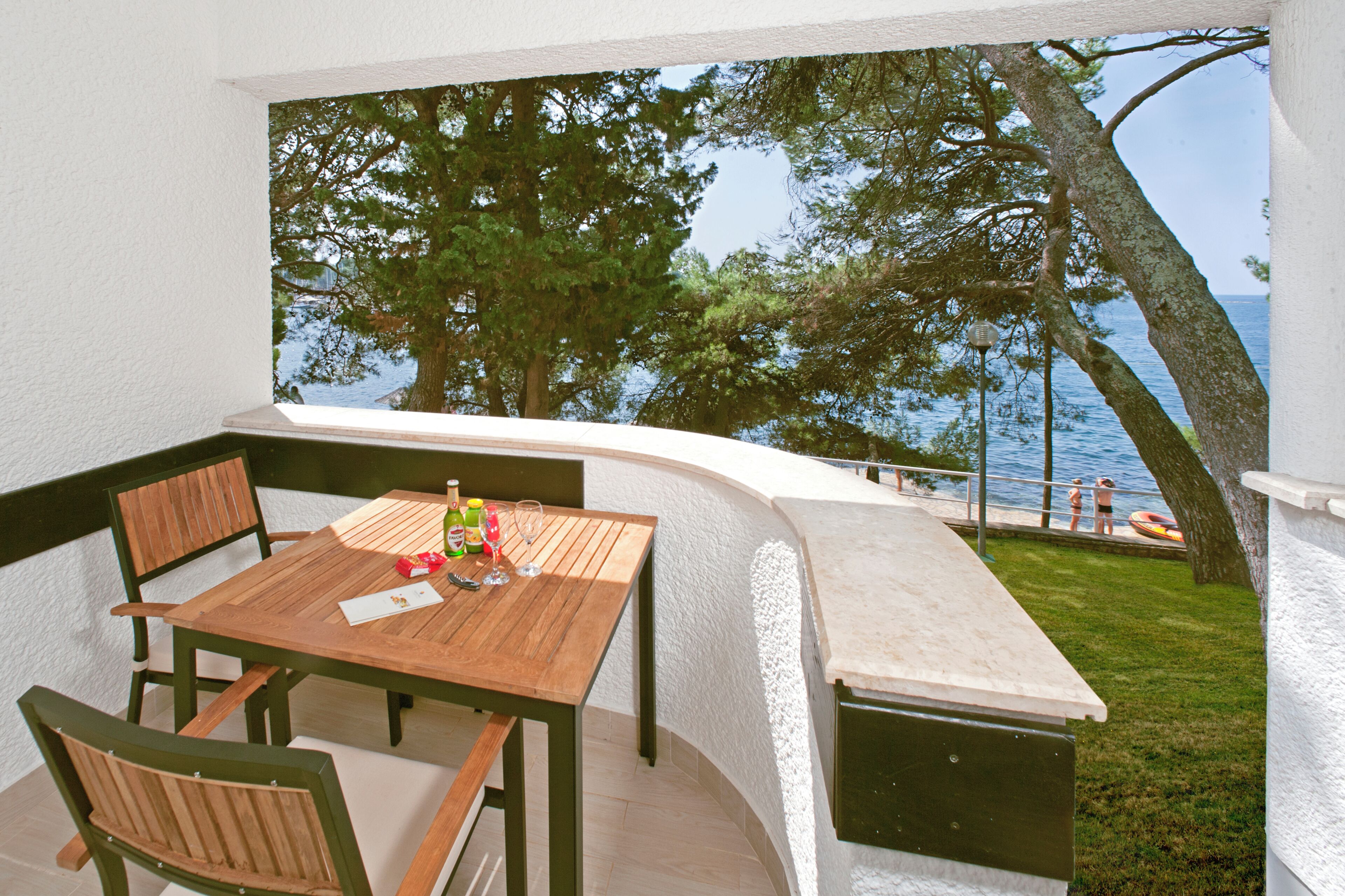 Une table et des chaises en bois sur un balcon donnant sur la mer et les arbres.