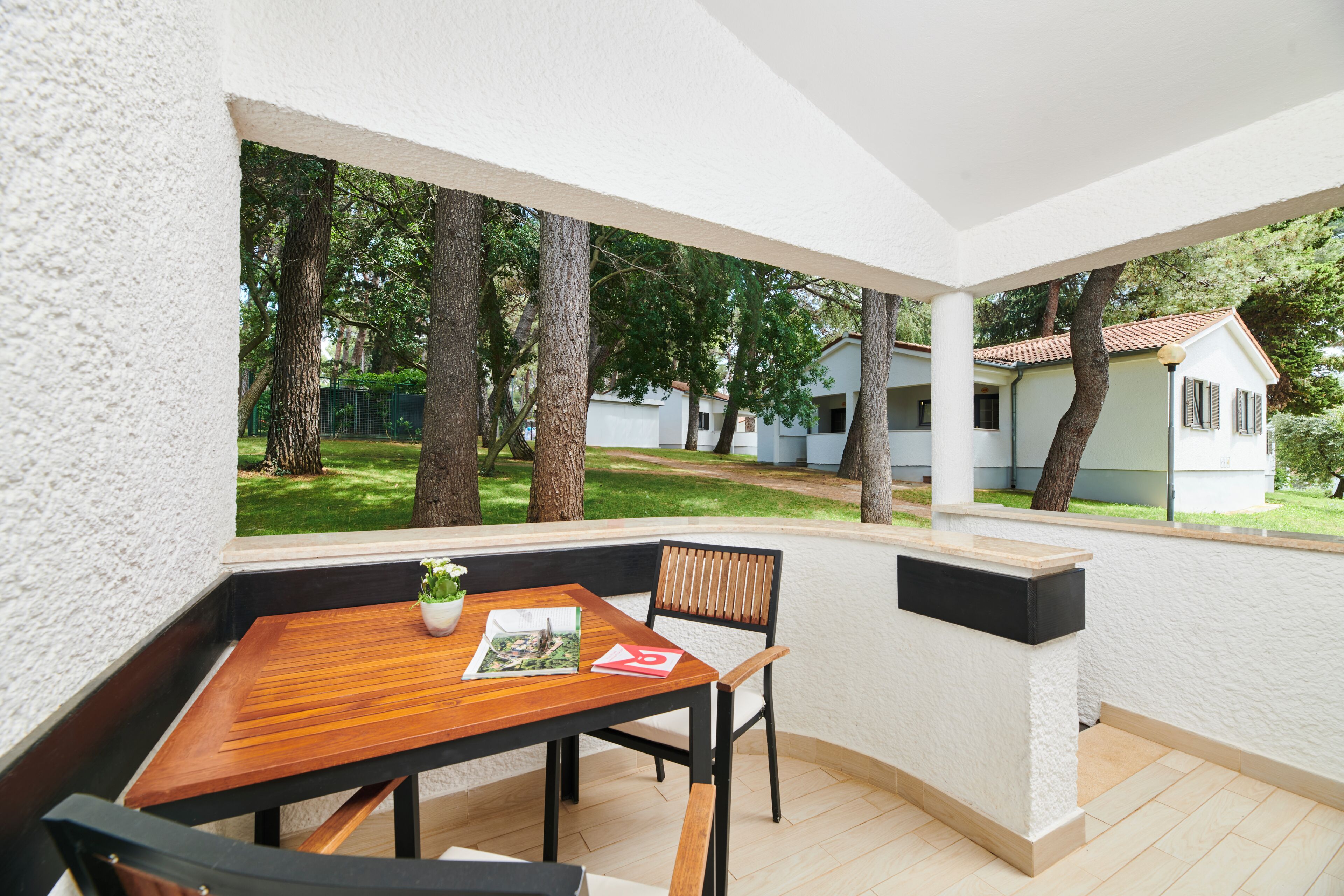 Une terrasse avec une table et des chaises en bois, un pot de fleurs et une vue sur un quartier résidentiel avec des arbres et des maisons.