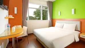 A hotel room with a bed, a desk, and a chair. There is a window with curtains, and the walls are painted in two colors. - Amaris Hotel Tebet (Jakarta)