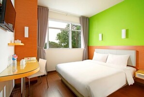 A hotel room with a bed, a desk, and a chair. There is a window with curtains, and the walls are painted in two colors. - Amaris Hotel Tebet (Jakarta)