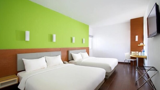 A hotel room with two beds, a desk, a chair, a TV, and a wall-mounted TV. - Amaris Hotel Tebet (Jakarta)