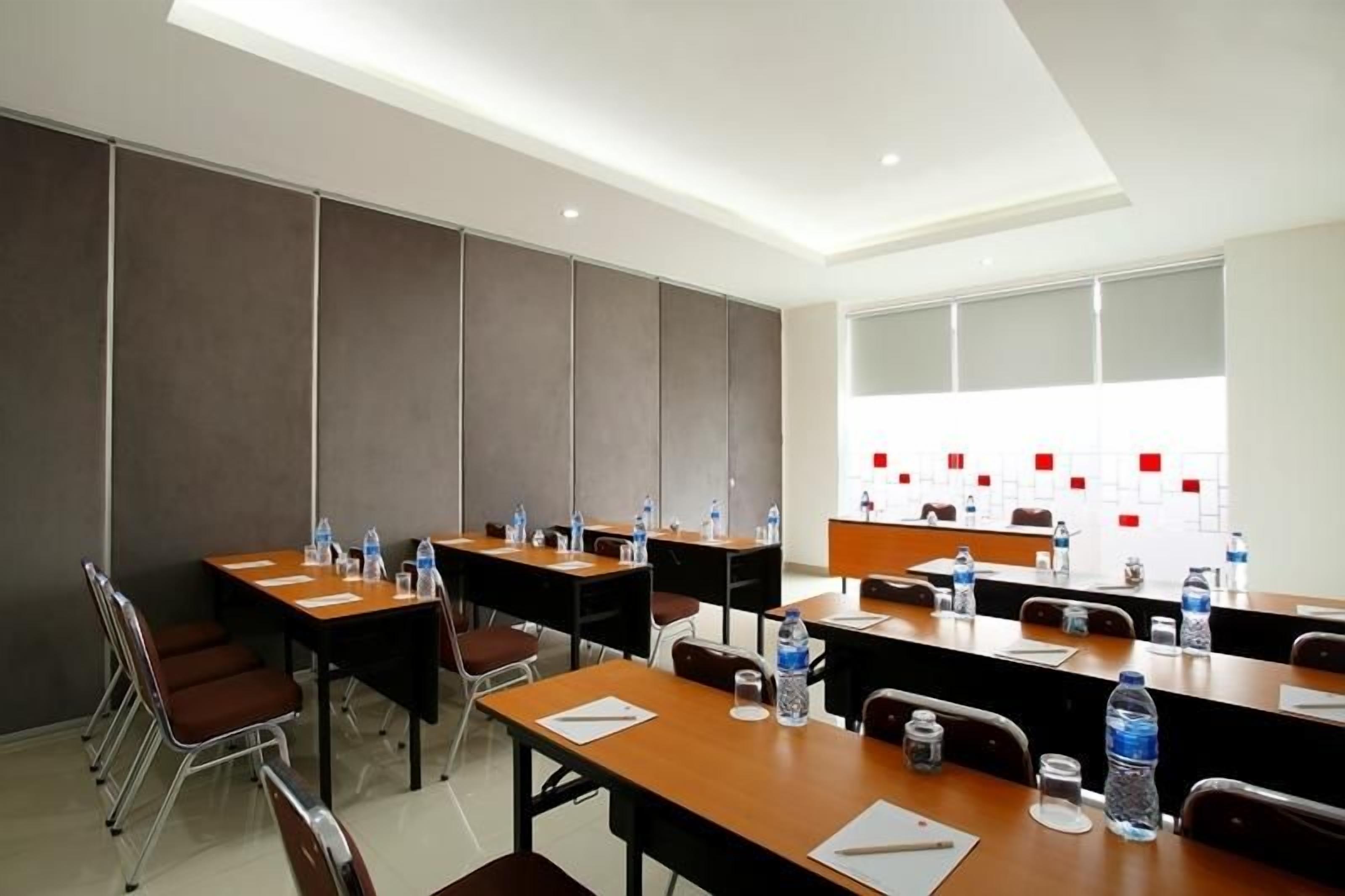 A conference room with multiple tables, chairs, and a long table with water bottles and papers.