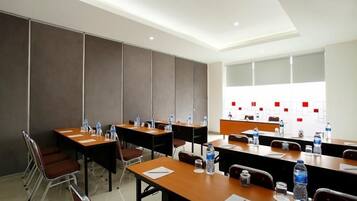 A conference room with multiple tables, chairs, and a long table with water bottles and papers.