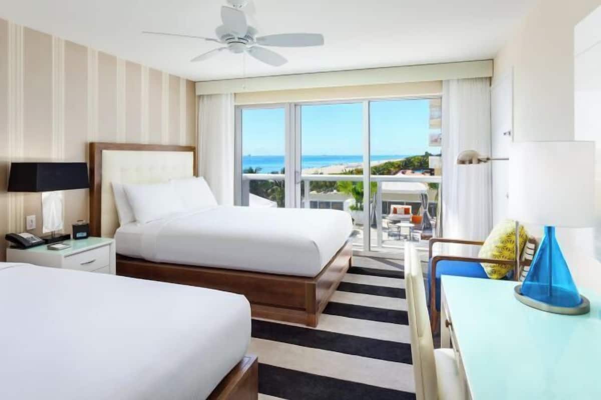 Habitación de hotel con cama, escritorio, silla, ventilador de techo y vista a la playa.