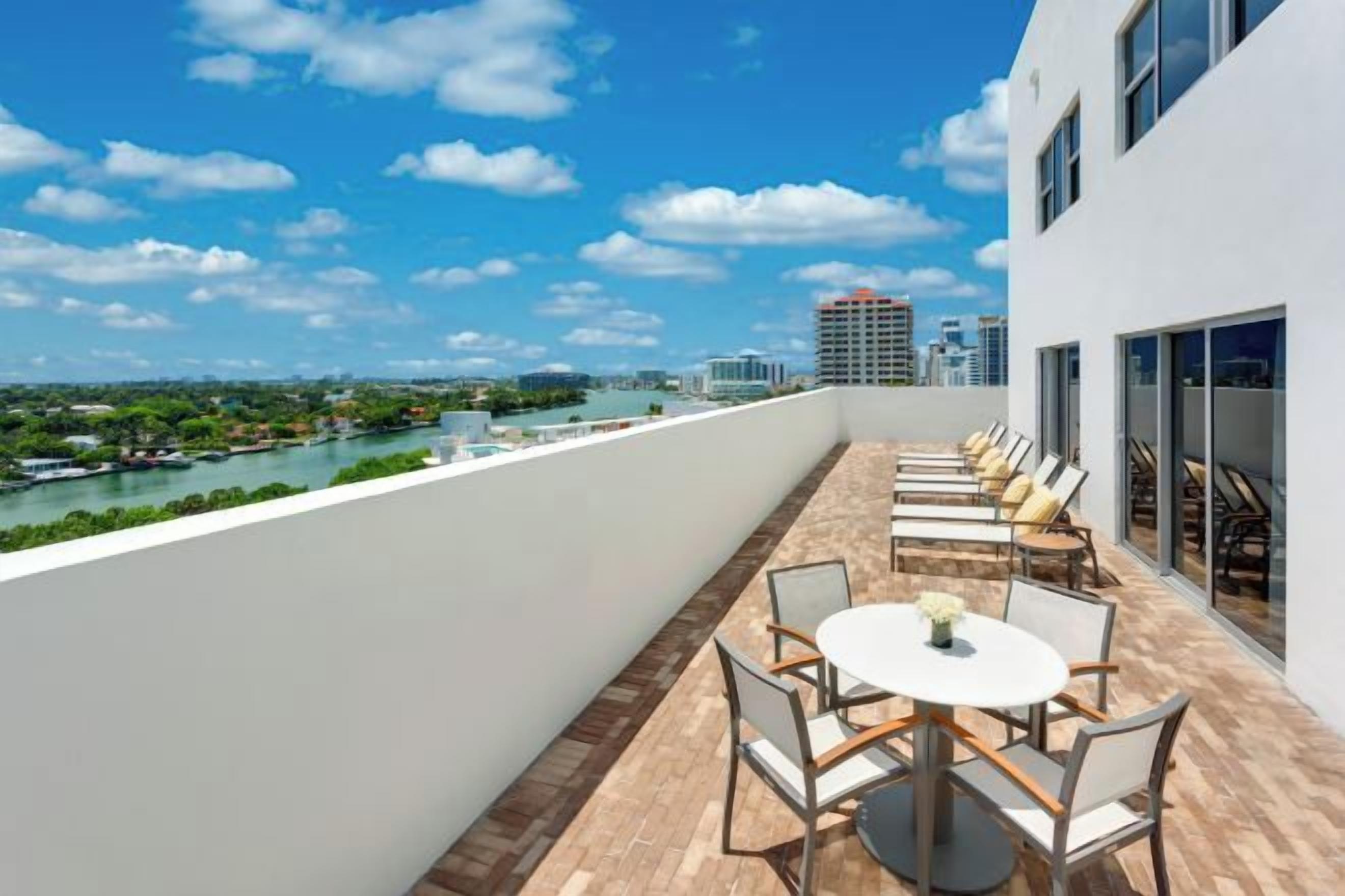 A rooftop terrace with a view of a river and city skyline, furnished with outdoor seating and a table.