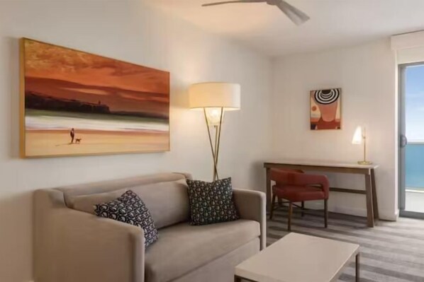 Un salon comprenant un canapé, une table basse, un bureau, une lampe et un tableau accroché au mur.