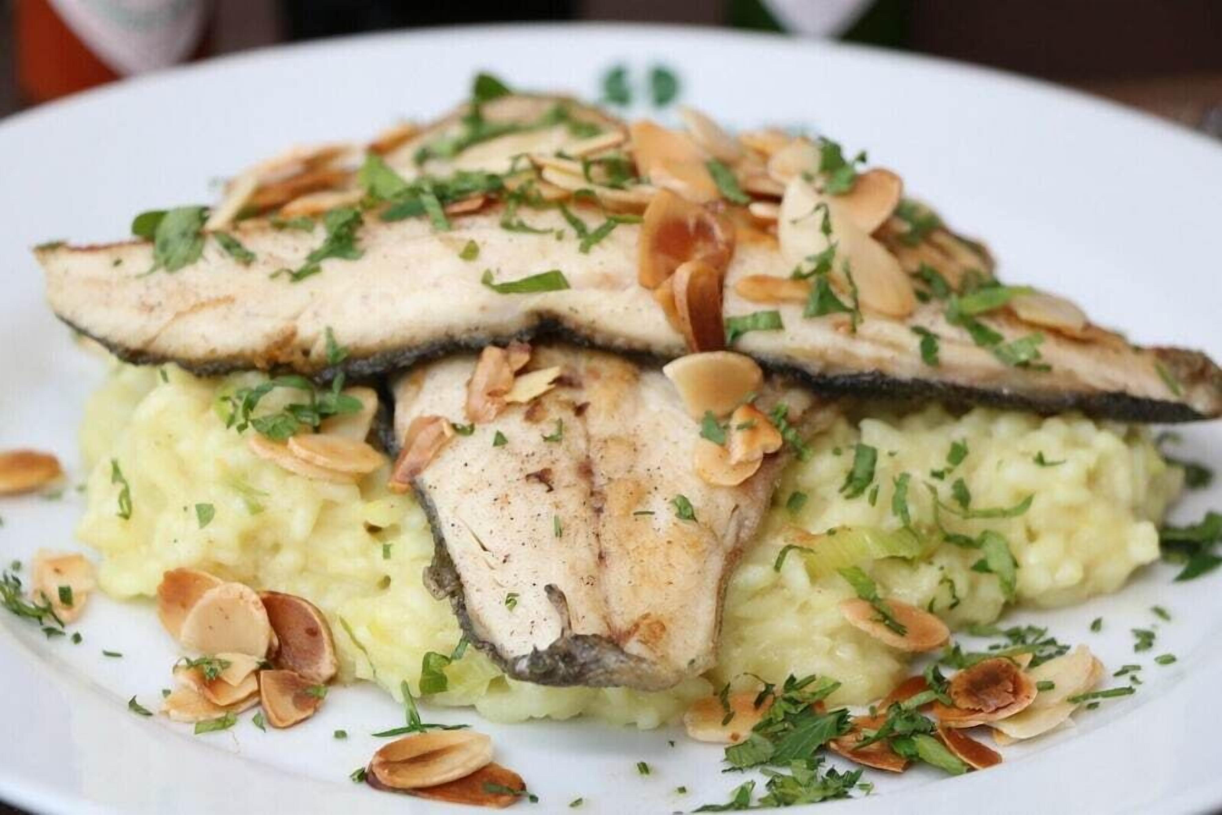 A plate of food with sliced fish on top of mashed potatoes, garnished with chopped herbs and sliced almonds.