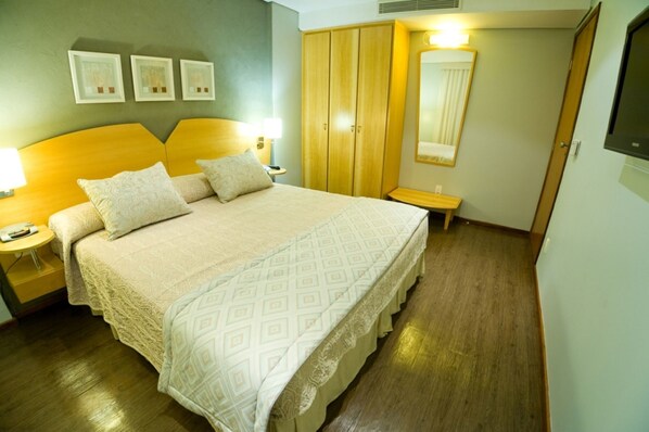Una habitación de hotel con una cama grande, un armario de madera, mesitas de noche y un espejo.
