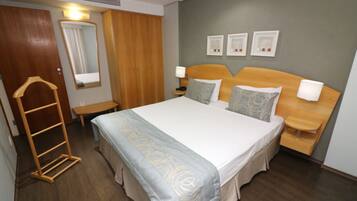 A hotel room with a large bed, wooden wardrobe, bedside tables with lamps, and three framed pictures on the wall.